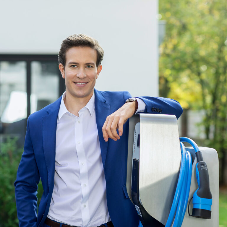 Ein E-Autofahrer lehnt an einer MENNEKES Wallbox